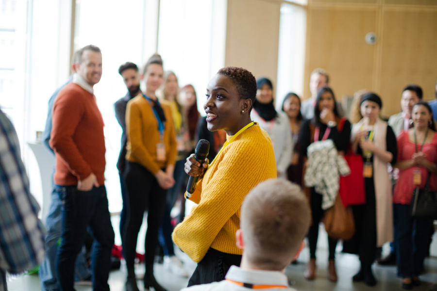 Smiling female speaker with microphone on stage leading group discussion